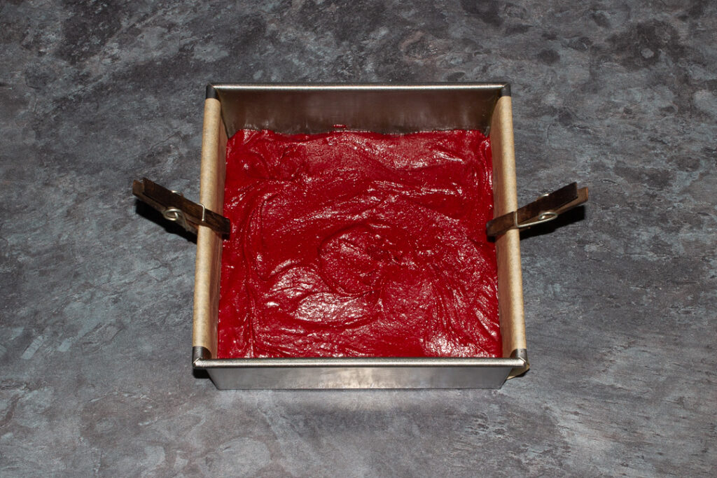 Red velvet brownie batter in a lined square tin.