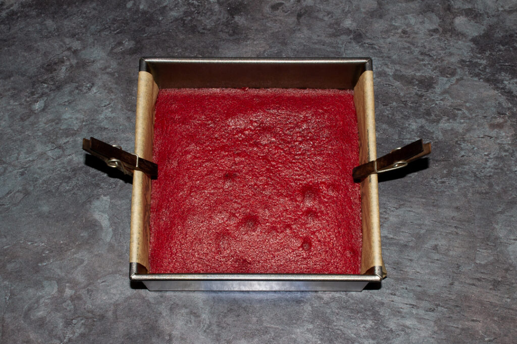 Baked red velvet brownie cooling in a lined square baking tin.