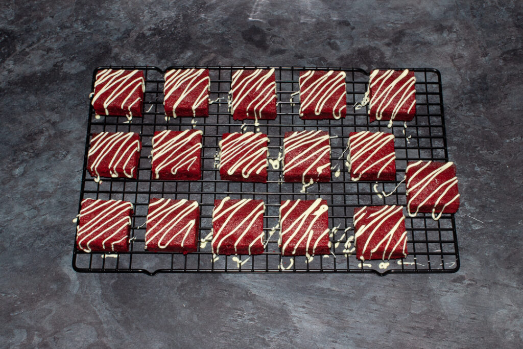 Red velvet brownies on a cooling rack that have been drizzled with melted white chocolate.