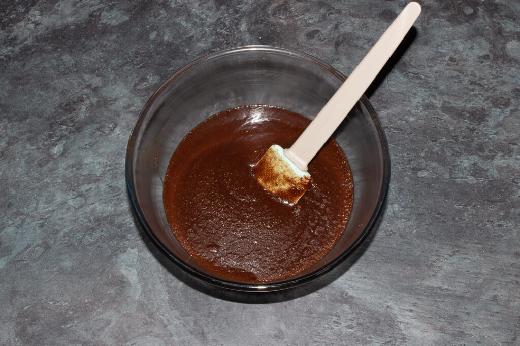 Melter butter, sugar and cocoa powder mixed together in a glass bowl with a spatula.