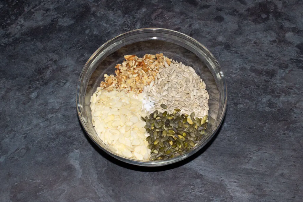 A glass bowl with all the dry homemade granola ingredients in it.