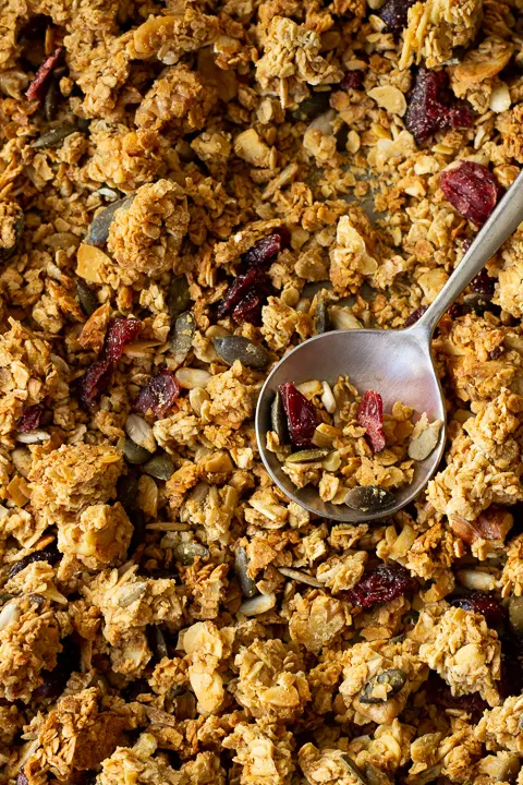 Birds eye view of homemade granola on a baking tray with a spoon on top.