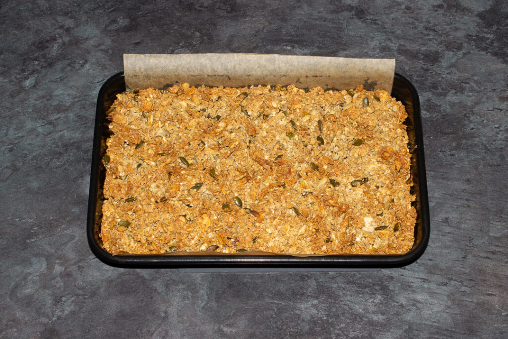 A lined rectangular tin with golden homemade granola inside.