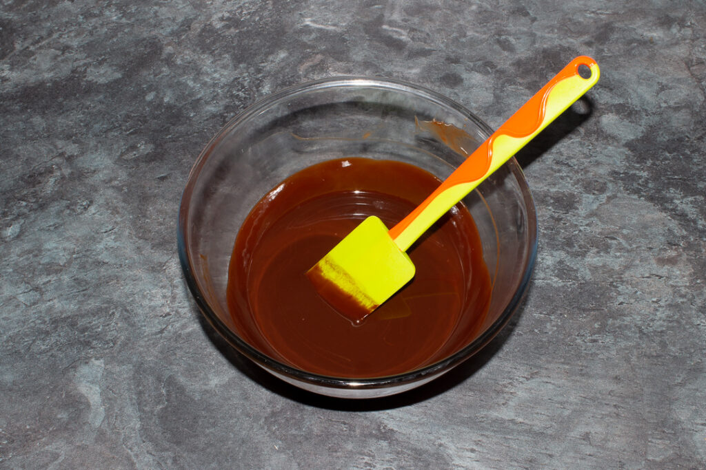 Melted butter and dark chocolate in a glass mixing bowl with a green spatula.