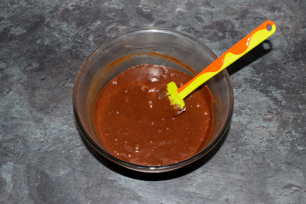 Twix brownie batter in a glass mixing bowl with a green spatula.