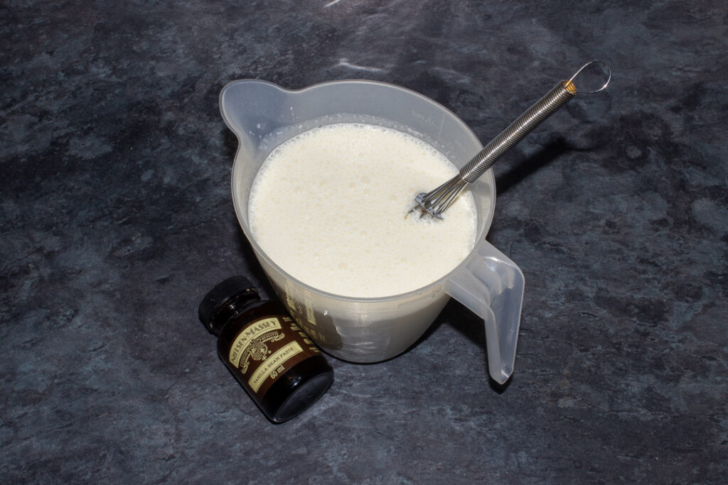 Double cream, milk, icing sugar and vanilla paste in a jug on a kitchen worktop.