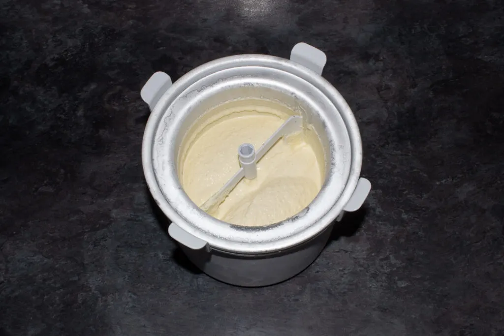 Vanilla ice cream in the bowl of an ice cream churner on a kitchen worktop.