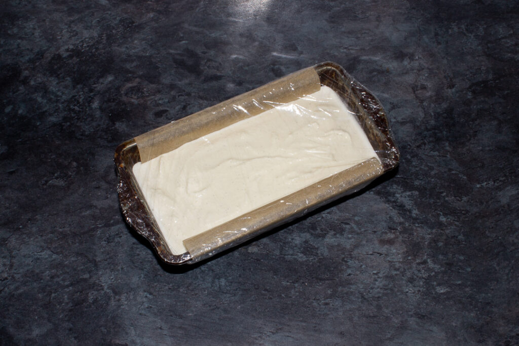Vanilla ice cream in a lined baking tin covered in cling film.