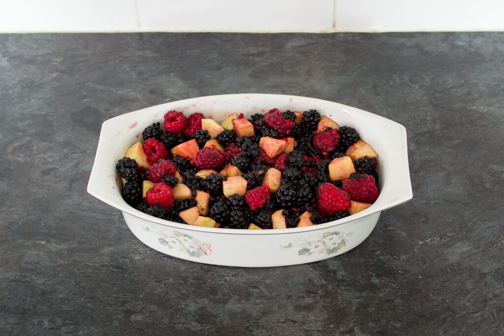 An oven proof dish filled with blackberries, raspberries and apples on a kitchen worktop.