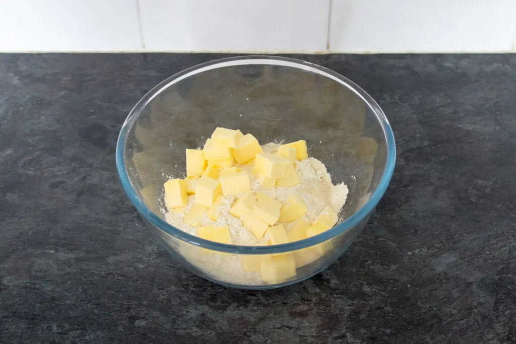 A glass bowl filled with cubed butter, flour salt and sugar on a kitchen worktop.
