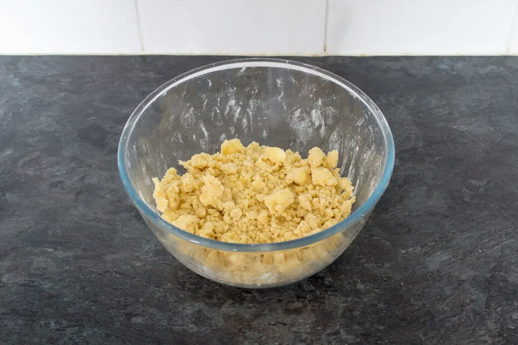 A glass bowl filled with a crumble mixture on a kitchen worktop.