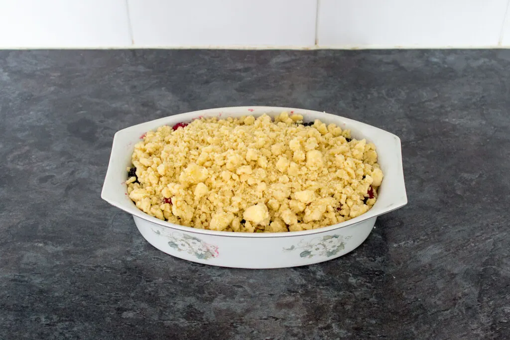 An oven proof dish filled with berries and apples then topped with a crumble mixture. Set on a kitchen worktop.