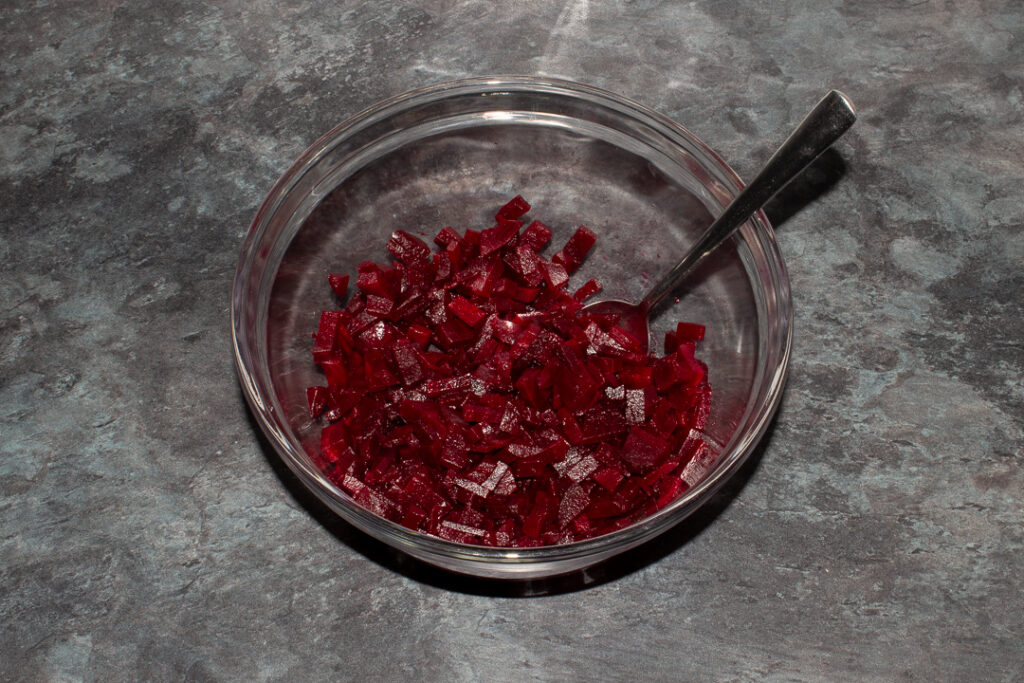 Diced beetroot in a mixing bowl with a spoon on a kitchen worktop.