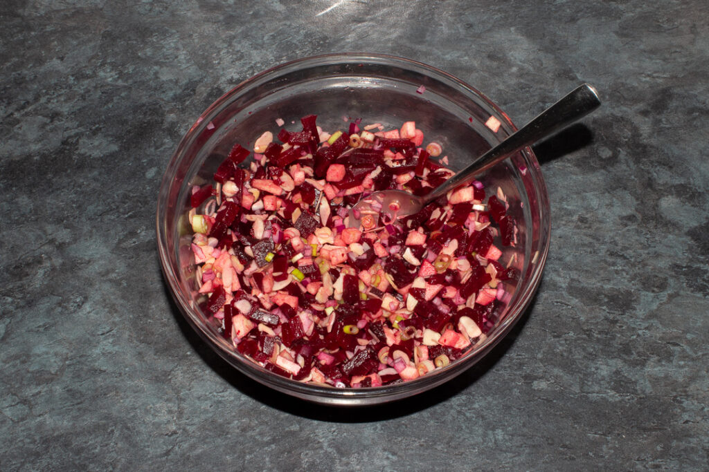 Apple and beetroot salad ingredients (minus the dressing) in a mixing bowl with a spoon inside on a kitchen worktop.
