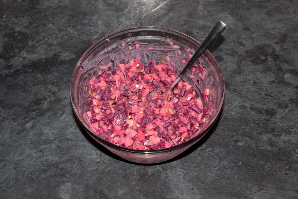 Apple and beetroot salad in a mixing bowl with a spoon on a kitchen worktop.