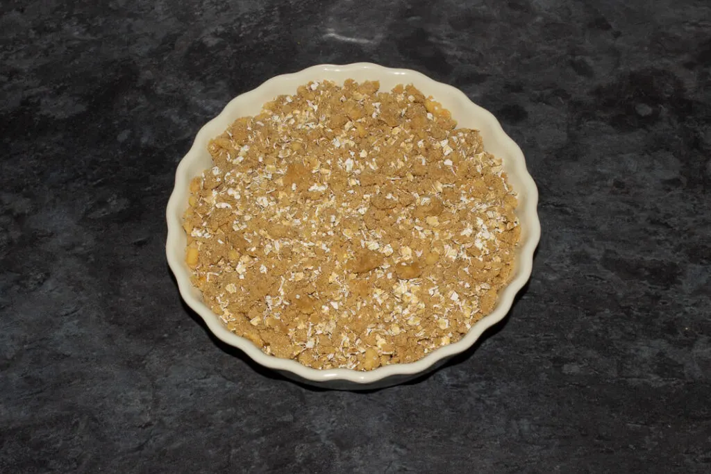 Peach mixture in a fluted ceramic serving dish topped with the crisp mixture.