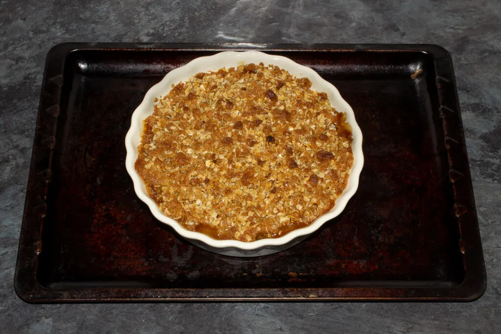 A baked peach crisp in a fluted ceramic serving dish set on a baking tray.