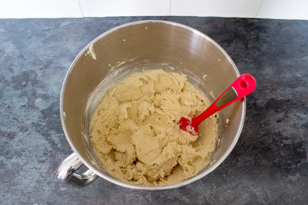 Creamed butter and sugar with egg and vanilla extract beaten in, in the bowl of an electric stand mixer on a kitchen worktop.