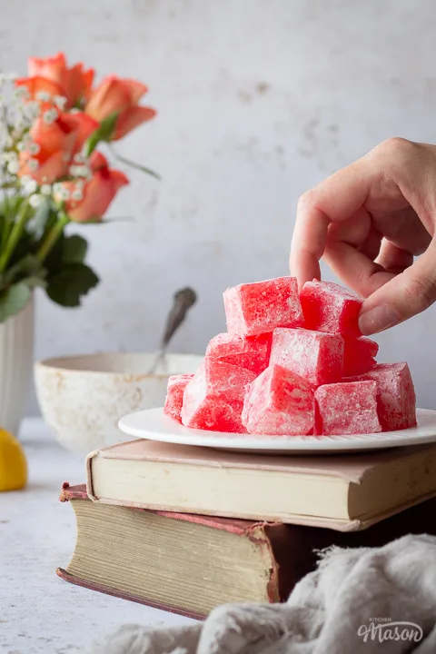 Someone taking a piece of Turkish delight from a plate on two stacked books
