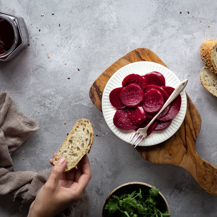 A white plate of pickled beetroot topped with a fork.