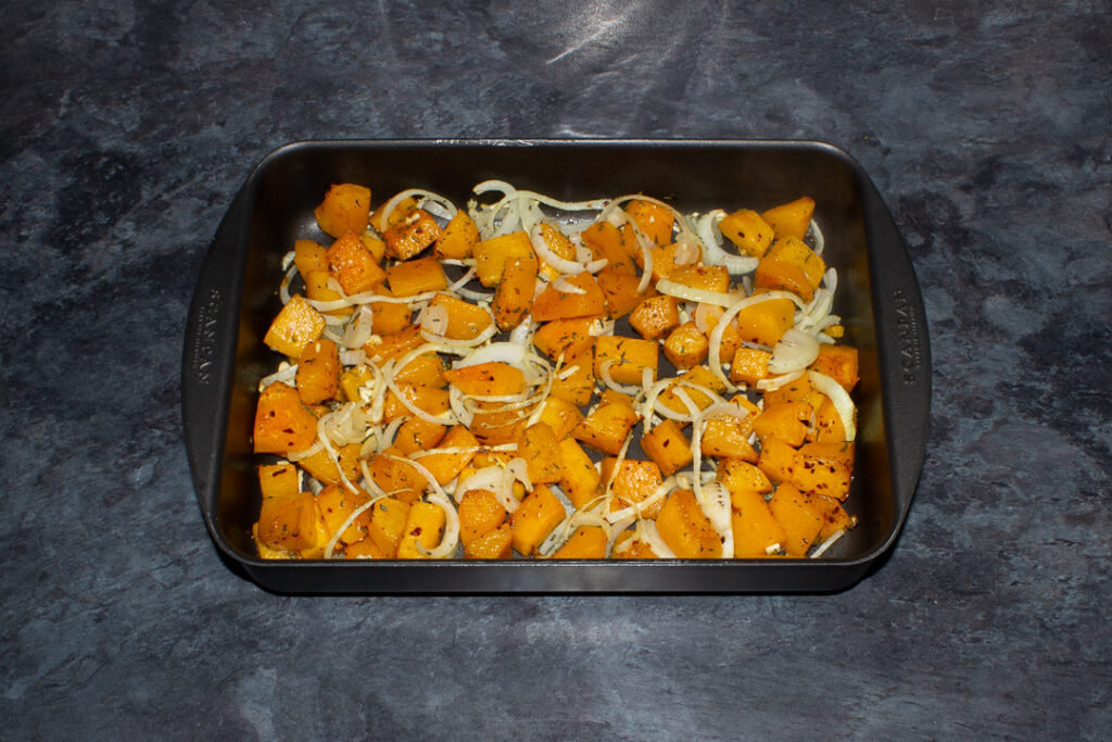 Cubes of roast chilli flake butternut squash, onion and garlic in a roasting pan. Set on a kitchen worktop.