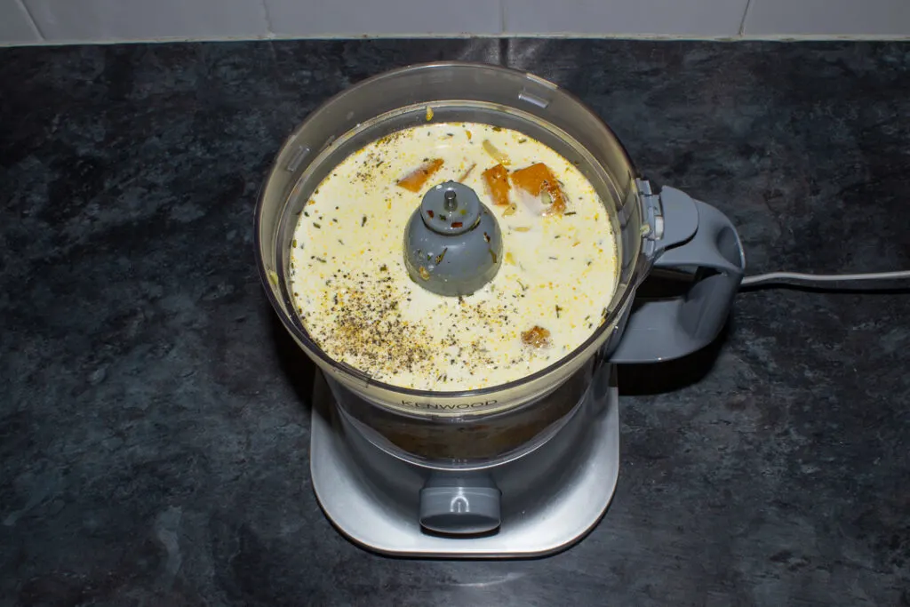 Spicy roast butternut squash ingredients in a blender set on a kitchen worktop.