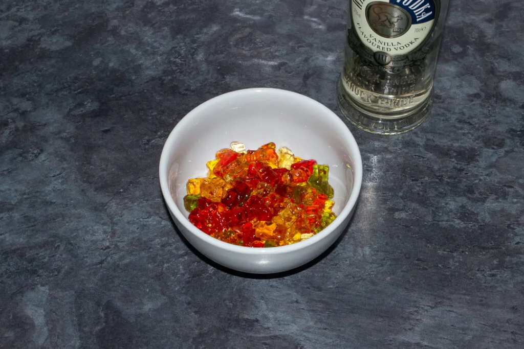 Rinsed vodka soaked gummy bears in a white bowl on a kitchen worktop. There's a bottle of vodka in the background.