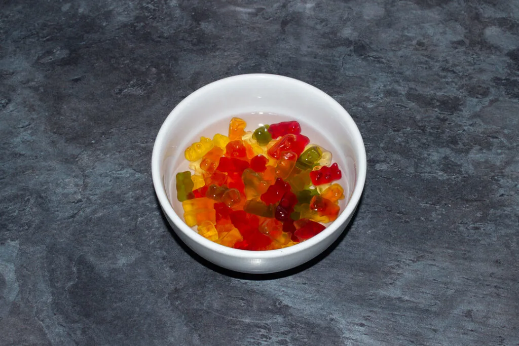 Gummy bears covered with vodka in a white bowl on a kitchen worktop.