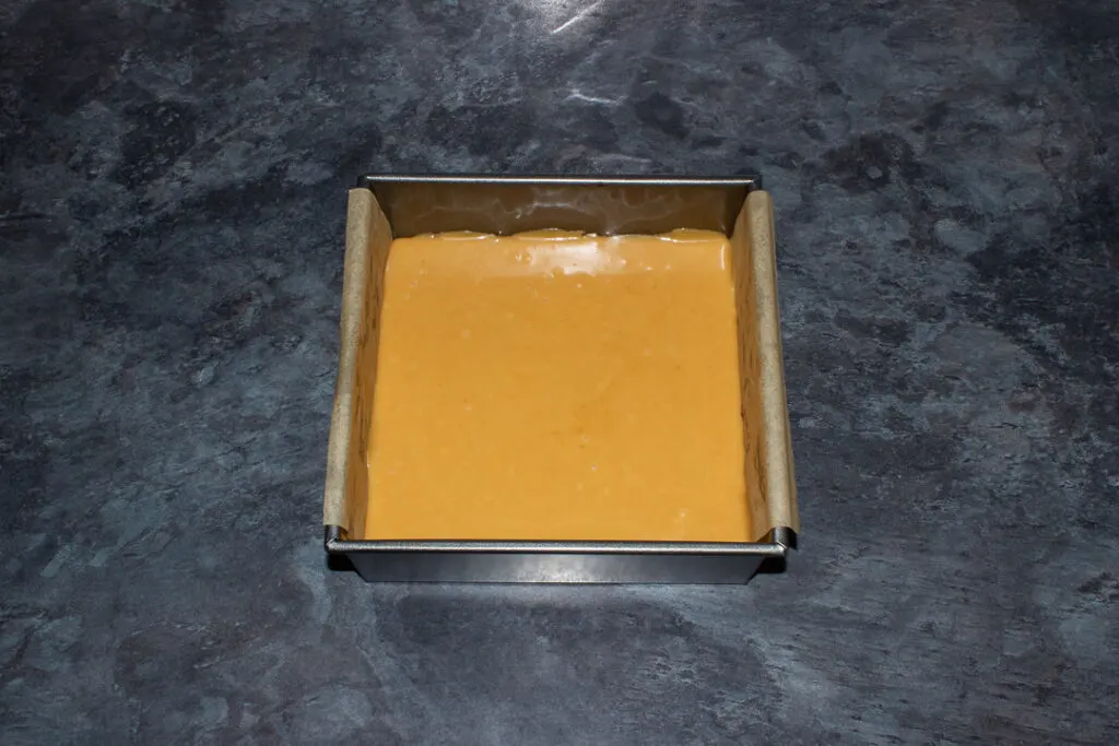 Caramel smoothed over a brownie base in a lined square baking tin on a kitchen worktop.