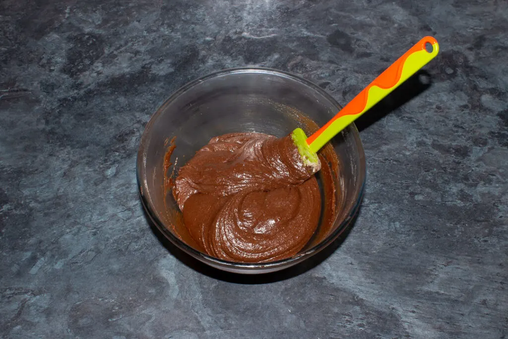 Brownie batter in a glass bowl on a kitchen worktop.