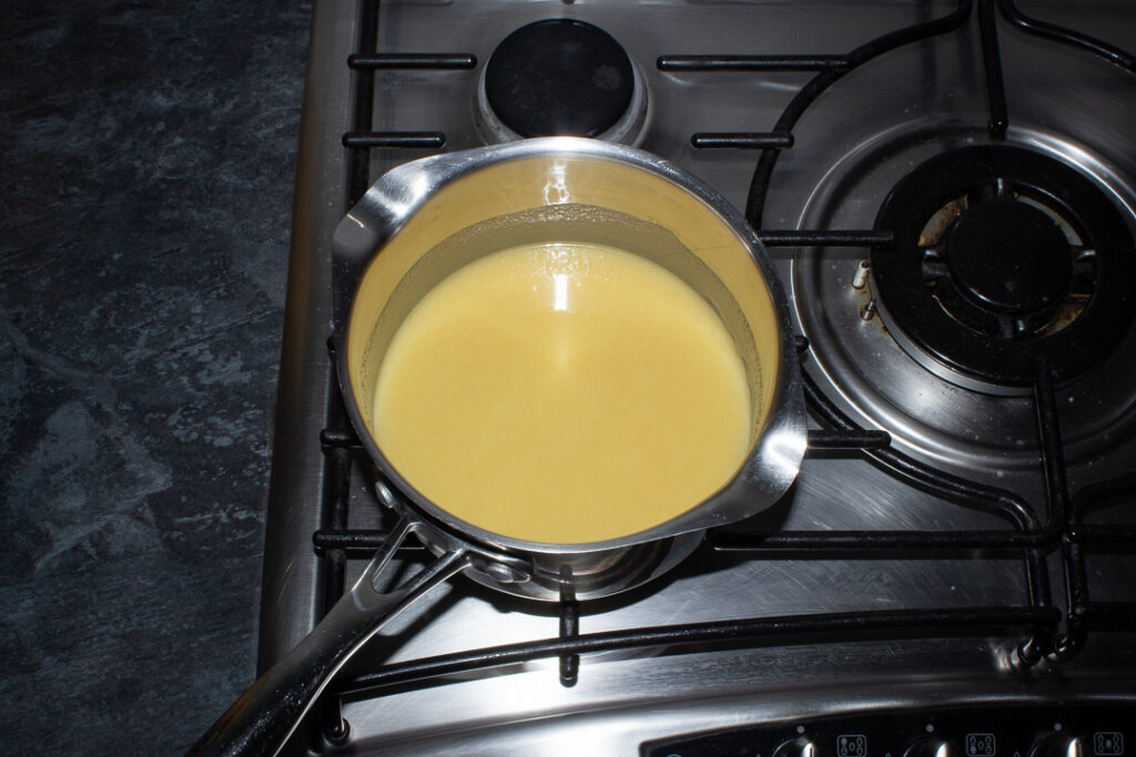 Caramel being brought to the boil in a saucepan set over a low heat on the stove top.