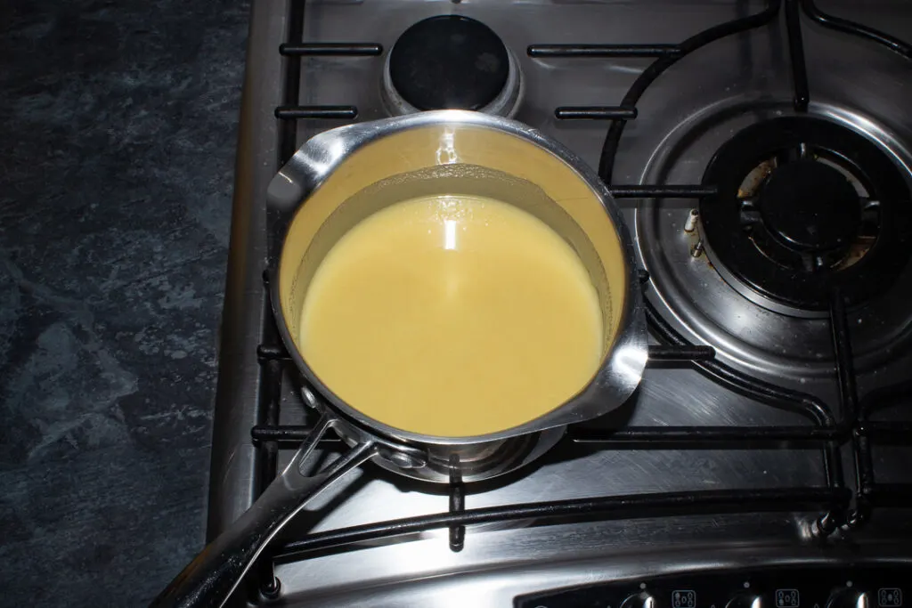 Caramel being brought to the boil in a saucepan set over a low heat on the stove top.