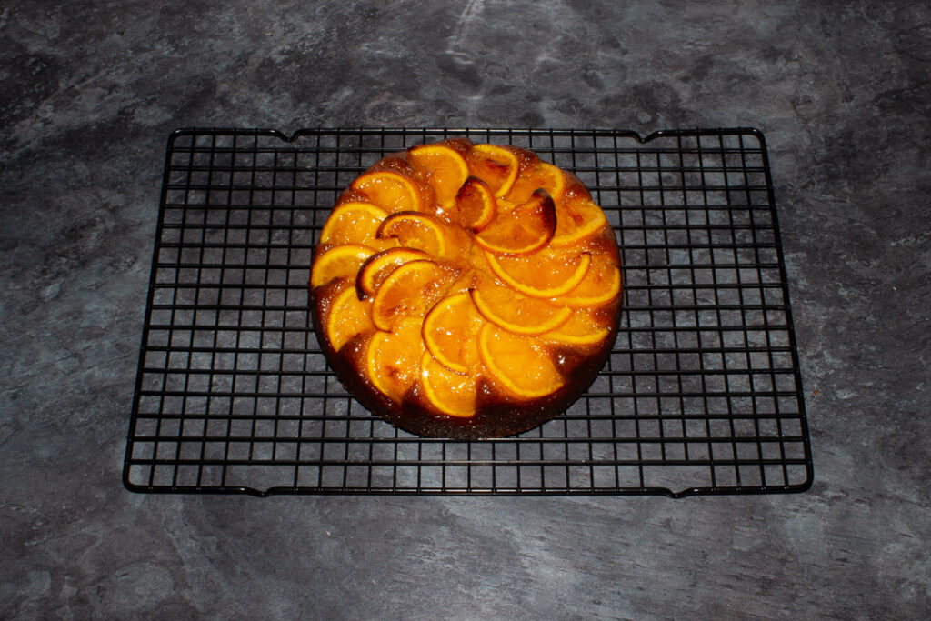 Baked sticky orange cake doused in orange syrup set on a cooling rack on a kitchen worktop.