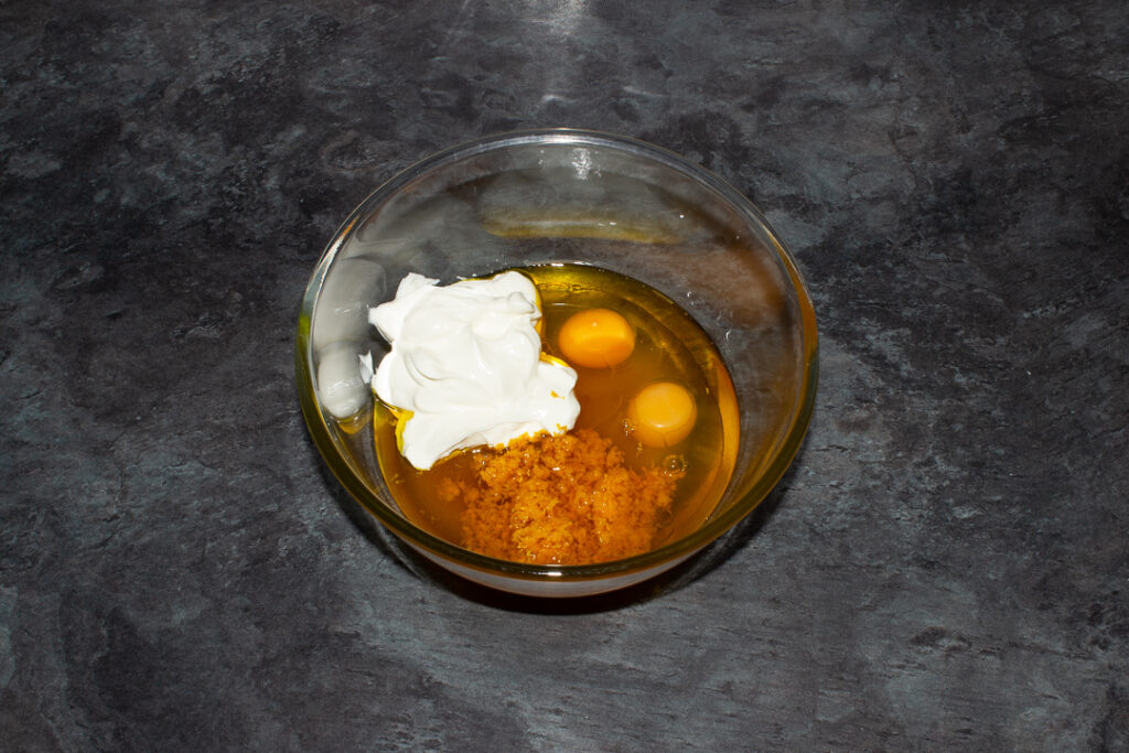 Sticky orange cake wet batter ingredients in a glass bowl on a kitchen worktop.