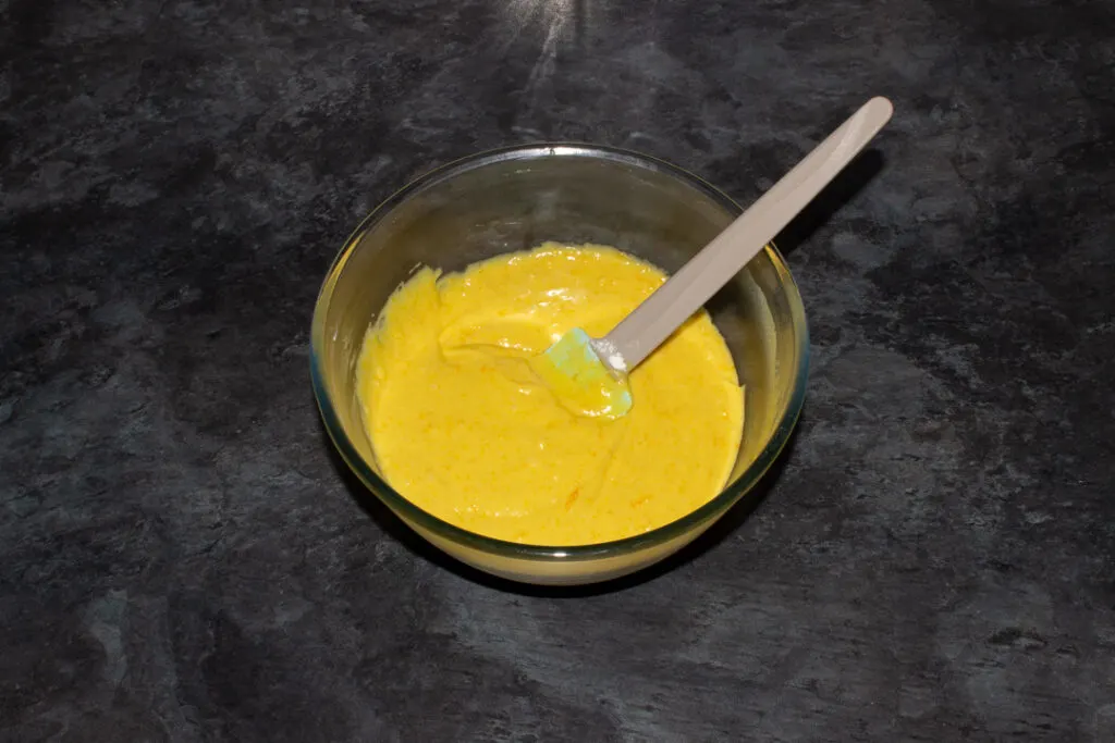 Sticky orange cake batter in a glass bowl with a spatula on a kitchen worktop.