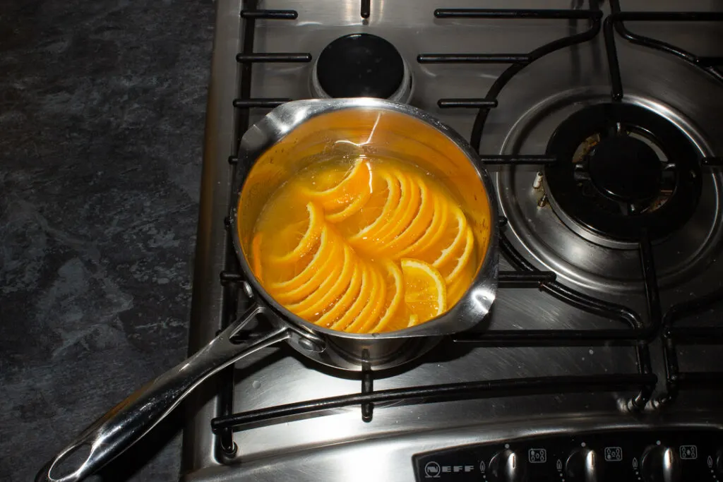 Semicircle orange slices, orange juice, sugar and water in a saucepan over a medium heat.