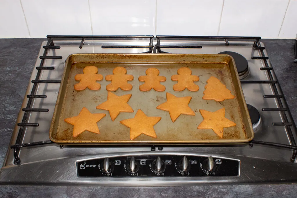 Baked gingerbread biscuits on a large baking tray on a kitchen worktop.