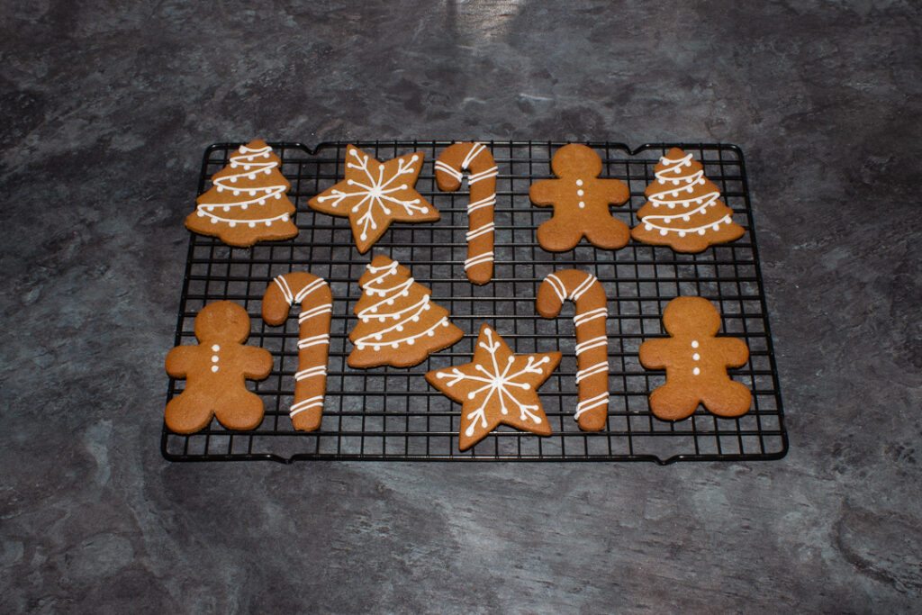 Decorated gingerbread biscuits on a cooling rack on a kitchen worktop.