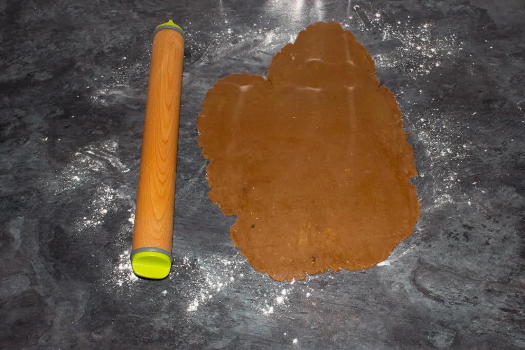 Gingerbread biscuit dough rolled out on a floured kitchen worktop with a rolling pin at the side.