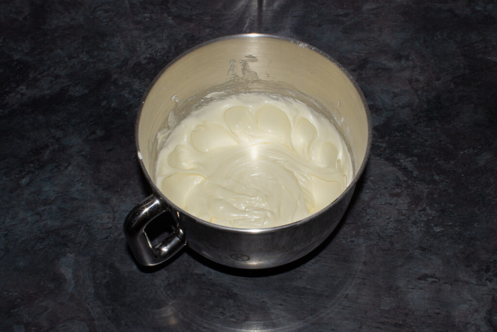 Cream cheese frosting without flavourings in a large silver bowl. Set on a kitchen worktop.
