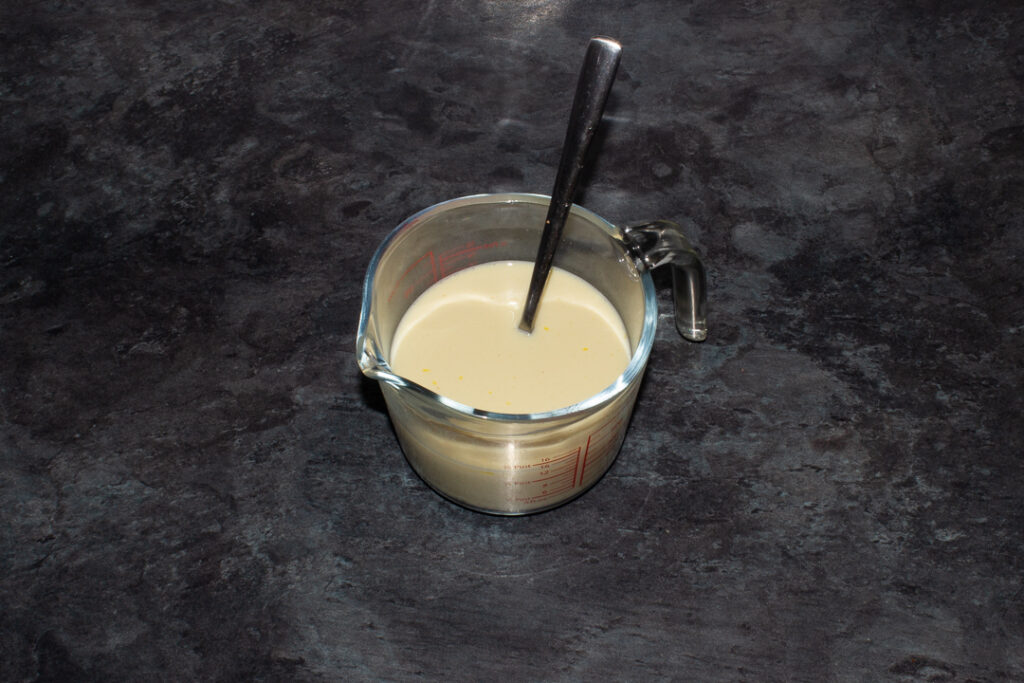 Milk, egg and vanilla mixed together in a jug with a fork in it. Set on a kitchen worktop.