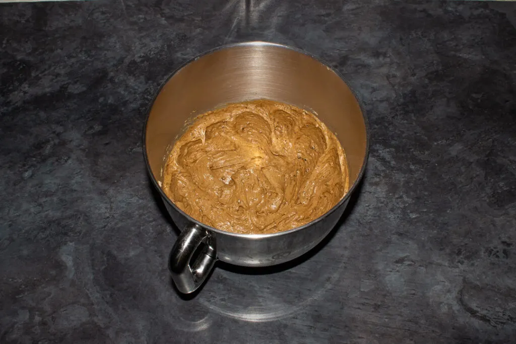 Gingerbread cupcake batter (with half the wet ingredients added) in a large silver bowl on a kitchen worktop.