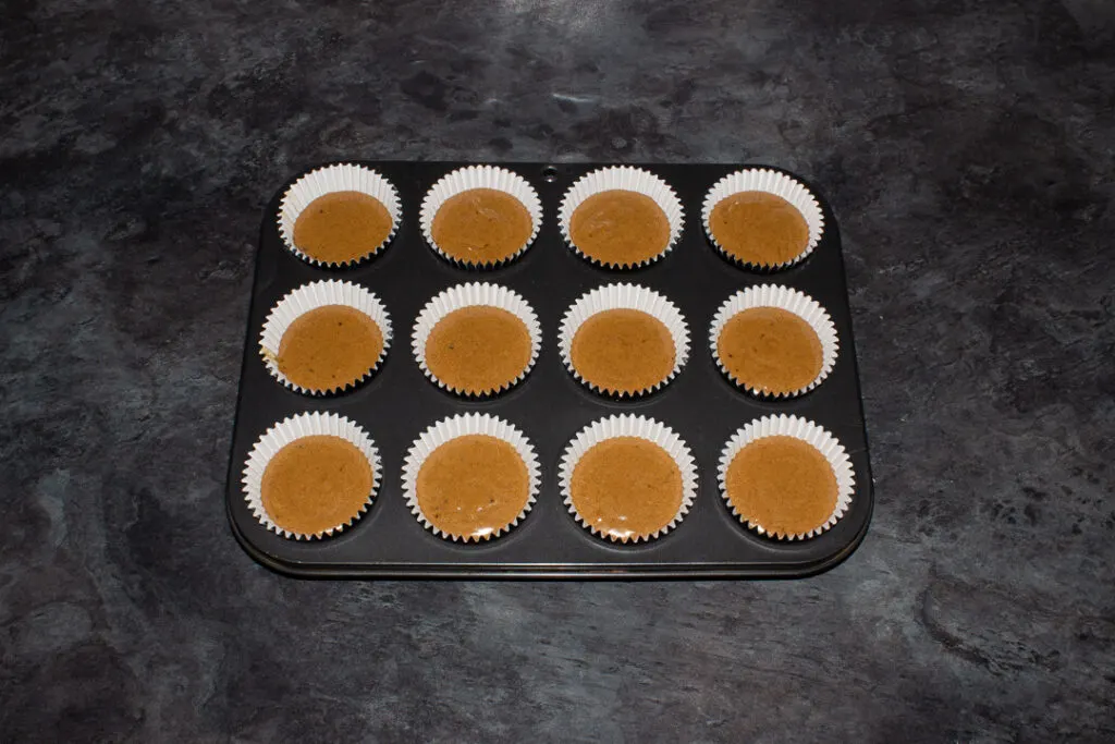 12 unbaked gingerbread cupcakes in a muffin tin set on a kitchen worktop.