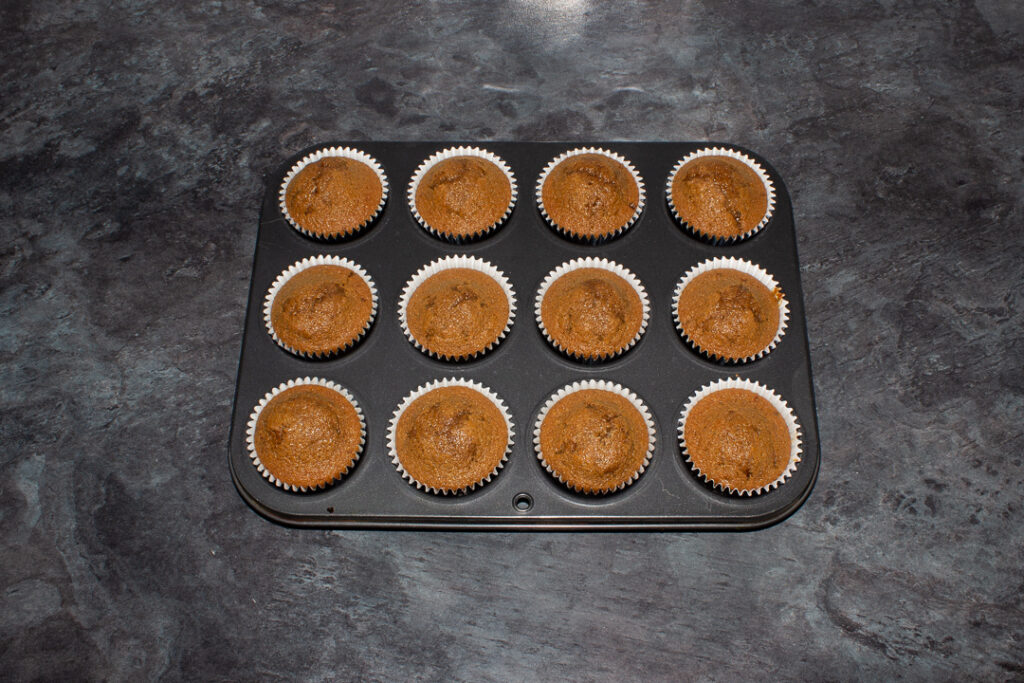 12 gingerbread cupcakes in a muffin tin set on a kitchen worktop.