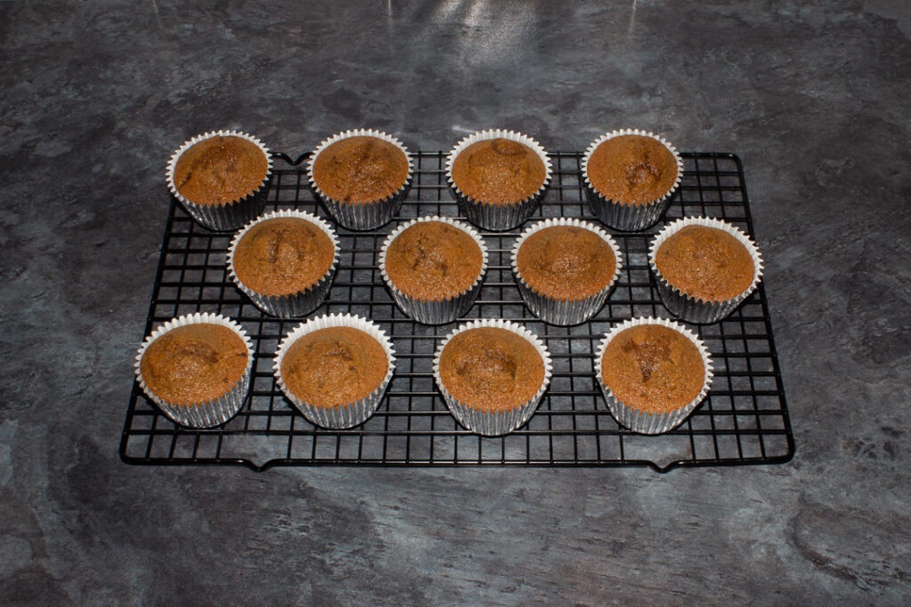 12 gingerbread cupcakes cooling on a wire rack on a kitchen worktop.