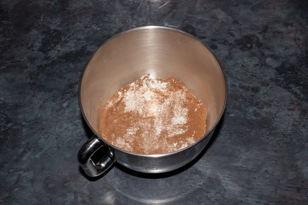 An electric stand mixer bowl on a kitchen worktop filled with flour, baking powder and cocoa powder.