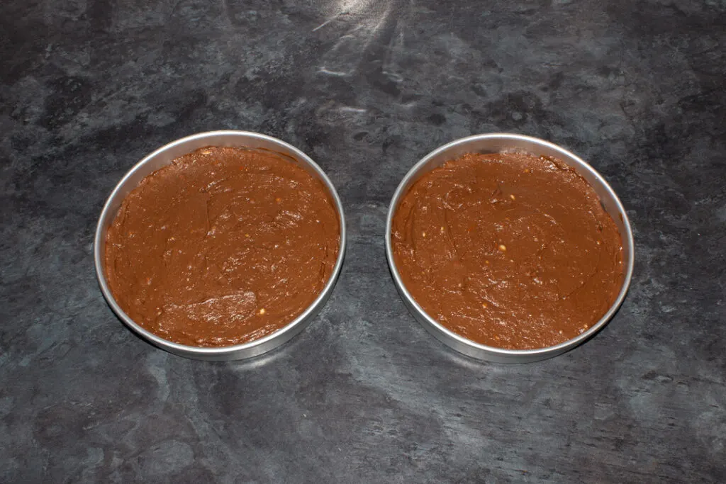 Two lined circular cake tins filled with chocolate orange cake batter on a kitchen worktop.