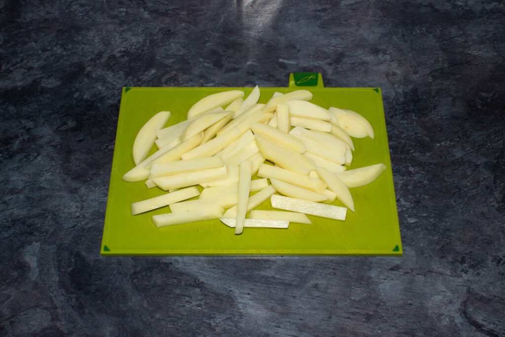 Peeled and sliced potatoes on a green chopping board set on a kitchen worktop.