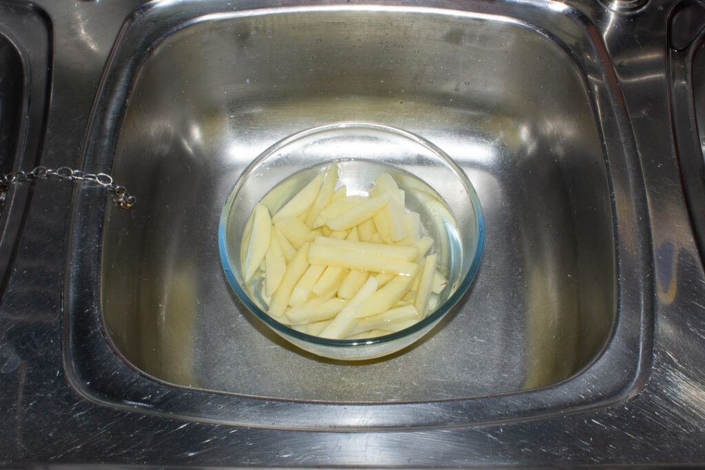 Uncooked chips in a large bowl of water in a sink.