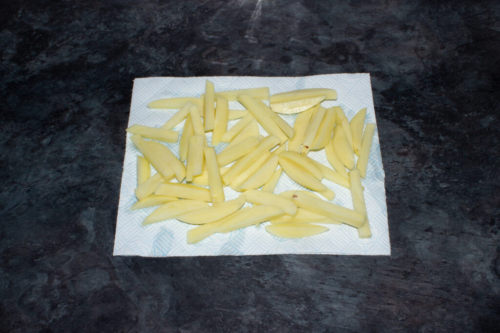 Uncooked chips that have been washed and are now being dried on kitchen roll on a kitchen worktop.
